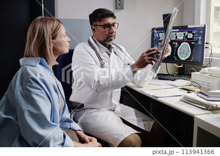 Biracial radiographer showing brain X-ray image to mature Caucasian female patient after CT procedure, copy space Biracial radiographer showing brain X-ray image to mature Caucasian female patient after CT procedure, copy space 113941366
