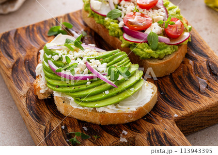 Avocado toasts with radishes, tomatoes and feta topped with olive oil 113943395
