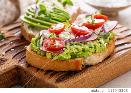 Avocado toasts with radishes, tomatoes and feta topped with olive oil 113943398