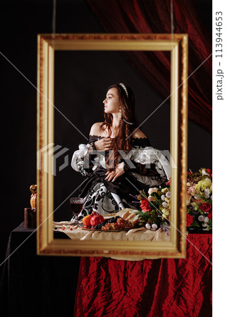 A woman in a Renaissance dress in a gold picture frame on a red background. A woman in a Renaissance dress in a gold picture frame on a red background. 113944653