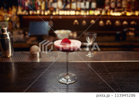 Pink cocktail decorated with rose floral petal on wooden bar counter desk Pink cocktail decorated with rose floral petal on wooden bar counter desk 113945286