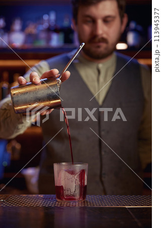 Elegant serious bartender pouring syrup from mix cup into glass Elegant serious bartender pouring syrup from mix cup into glass 113945377