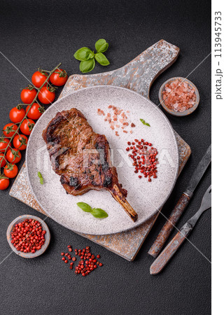 Delicious juicy beef steak on the bone, tomahawk with salt, spices and herbs Delicious juicy beef steak on the bone, tomahawk with salt, spices and herbs 113945733