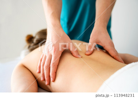 Girl during back massage in spa salon. Masseur hands doing care body therapy procedure for young woman wellness and relaxation. 113948231