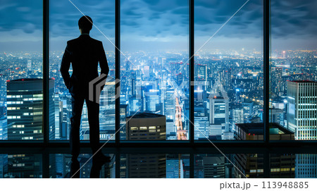 A man in a suit stands in front of a window looking out at the city 113948885