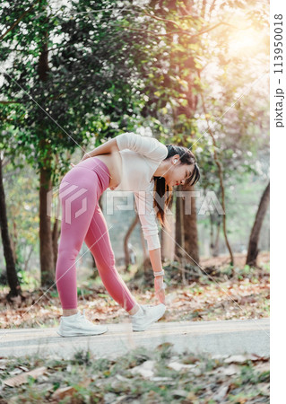 Active young woman taking a break to stretch her legs in a sunlit forested park. 113950018