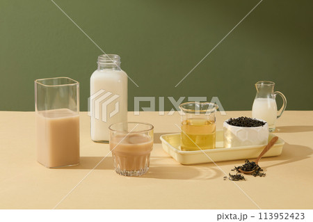 Forest green background against a few glasses and cup filled with drinks inside on beige table. Copy space, photo for beverage, beauty or cosmetic presentation Forest green background against a few glasses and cup filled with drinks inside on beige table. Copy space, photo for beverage, beauty or cosmetic presentation 113952423
