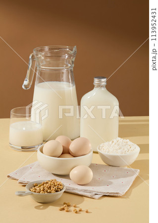 Brown and beige tone with a set of ingredient baking, a unlabeled glass bottle of soy milk beside many other ingredients such as eggs, flour, soybean. Photo with blank space for cooking or baking conc 113952431