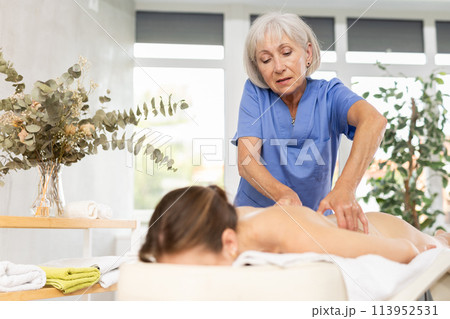 Elderly woman doing back massage to young woman Elderly woman doing back massage to young woman 113952531