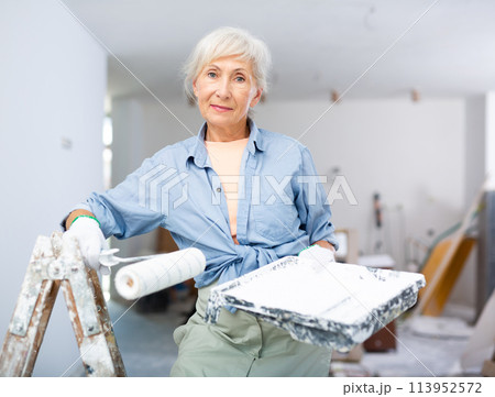 Mature woman painting walls with paint roller in refurbished room 113952572