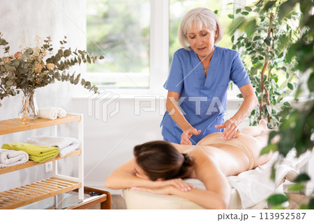 Unrecognizable young woman lies face down and enjoy lower back massage, spa body care Unrecognizable young woman lies face down and enjoy lower back massage, spa body care 113952587