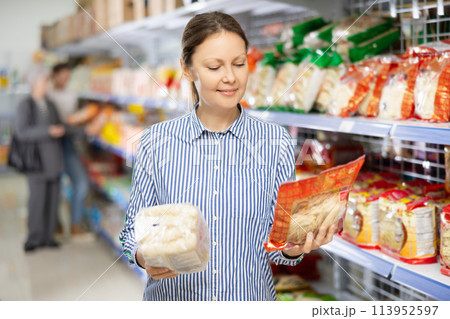 Interested female shopper choosing noodles at Asian grocery store Interested female shopper choosing noodles at Asian grocery store 113952597