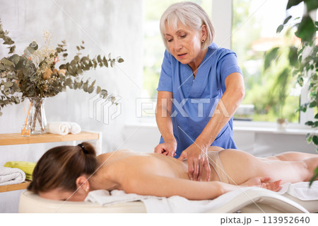 Skilled aged masseuse doing back pain relief massage to young woman 113952640