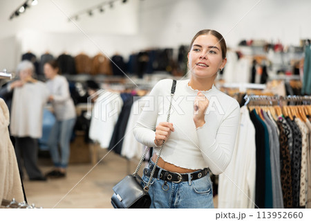 Positive joyful young woman looking for fashionable clothes in clothing boutique 113952660