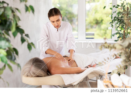 Unrecognizable elderly woman lies face down on couch and enjoy spa treatments, shoulder massage 113952661