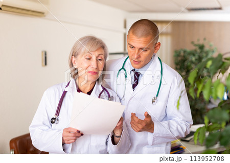Two professional doctors discussing medical card of patient 113952708