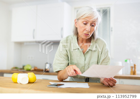 Worried mature woman checking papers at home Worried mature woman checking papers at home 113952799