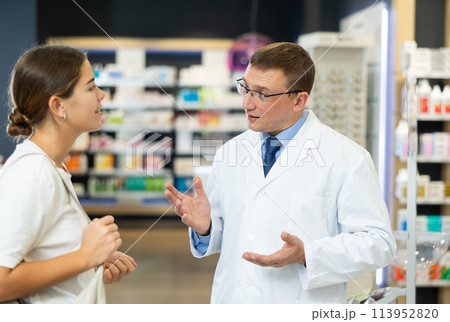 Pharmacist man communicates with girl visiting pharmacy 113952820