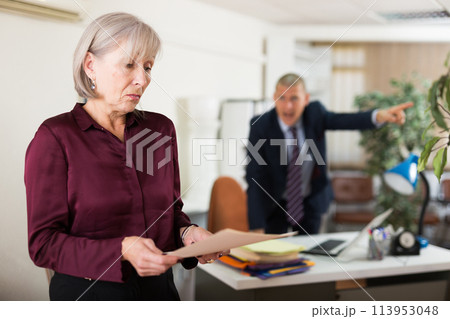 Frustrated female office employee with paper on background of disgruntled manager Frustrated female office employee with paper on background of disgruntled manager 113953048