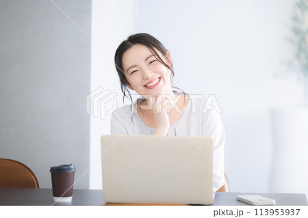 デスクに座ってパソコンをしながらカメラ目線の笑顔の若いかわいい女性　 113953937