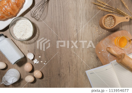 Photo of ingredients and utensils for home baking decorated with wheat, notebook, croissant, egg, milk, flour and so on. Top view with blank space in the middle for displaying product or adding text Photo of ingredients and utensils for home baking decorated with wheat, notebook, croissant, egg, milk, flour and so on. Top view with blank space in the middle for displaying product or adding text 113954077