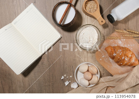 A blank notebook opened beside ingredients for baking cake or pastry flat lay on wooden kitchen counter top. Space for designing, top view A blank notebook opened beside ingredients for baking cake or pastry flat lay on wooden kitchen counter top. Space for designing, top view 113954078