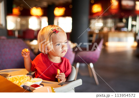 Little girl on a highchair with french fries in her hands. High quality photo Little girl on a highchair with french fries in her hands. High quality photo 113954572
