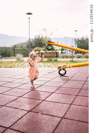 Little girl walks along the rubber surface of the playground to the swing-balancer. High quality photo Little girl walks along the rubber surface of the playground to the swing-balancer. High quality photo 113954638