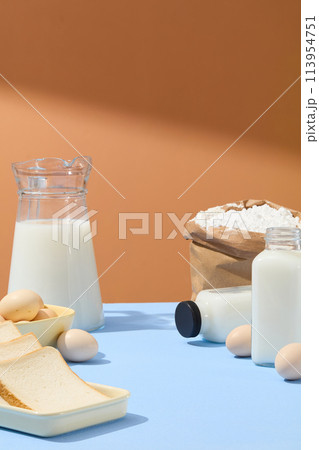 Concept of breakfast or baking with a bag containing flour decorated with some eggs in a bowl and a dish of sandwiches. Blank space in the middle for product advertising Concept of breakfast or baking with a bag containing flour decorated with some eggs in a bowl and a dish of sandwiches. Blank space in the middle for product advertising 113954751