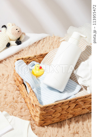 Template for baby bath accessories advertising, a rattan basket contains products for baby bath, a rubber duck, a blue striped towel and a blank label bottle. Top view photo, copy space Template for baby bath accessories advertising, a rattan basket contains products for baby bath, a rubber duck, a blue striped towel and a blank label bottle. Top view photo, copy space 113955472