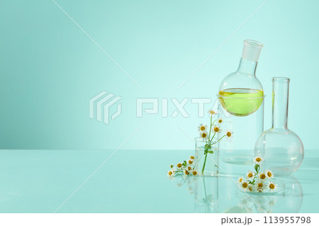 Laboratory glassware, beaker, boiling flask made of transparent glass with yellow fluid on light blue background. Daisy Flower Extract is a non-toxic used to brighten skin and prevent hyperpigmentatio Laboratory glassware, beaker, boiling flask made of transparent glass with yellow fluid on light blue background. Daisy Flower Extract is a non-toxic used to brighten skin and prevent hyperpigmentatio 113955798