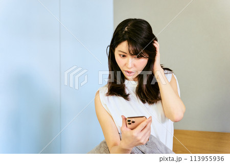 起床時にスマートフォンで時間を確認し寝坊し出勤時間に遅刻しそうな30代の1人暮らしの日本人の女性 113955936