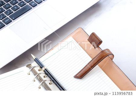 リング式のシステム手帳を開いて、ノートパソコンでデスクワークをしている会社員のイメージ 113956783