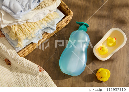 Baby care theme in rustic concept, a empty label blue bottle lay by a some rubber yellow ducks on wooden background, decorated by rattan basket of baby clothes. Space for advertising and copy space Baby care theme in rustic concept, a empty label blue bottle lay by a some rubber yellow ducks on wooden background, decorated by rattan basket of baby clothes. Space for advertising and copy space 113957510