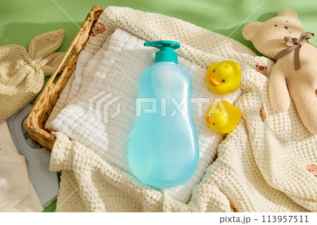 Template for baby products advertising, green background against knitted towel, a rattan basket contains a linen towel below a blue bottle without label. Top view, mockup for design 113957511