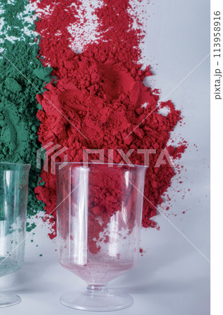 Red and green holi powder in a measuring cup on white background. 113958916