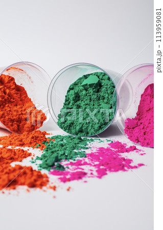 Three Glass bowl leaning against a white background with multicolored holi powders scattered from it. 113959081