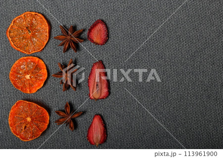 Tangerines are cut into slices and dried to decorate desserts. Nearby are stars of anise and strawberry slices. On a gray background. 113961900