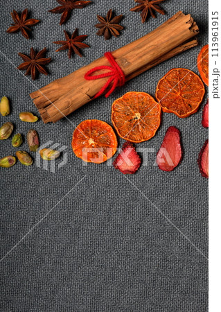 Dried tangerines and strawberries, cut into pieces to decorate the dessert. Nearby are pistachios, anise and cinnamon sticks tied with red thread. On a gray background. 113961915