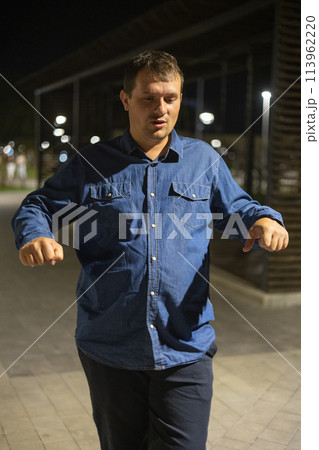 Talking to his friends at night in the park, a man gesticulates and shows something. A guy explains something to his friends in a city park on a summer night. Talking to his friends at night in the park, a man gesticulates and shows something. A guy explains something to his friends in a city park on a summer night. 113962220