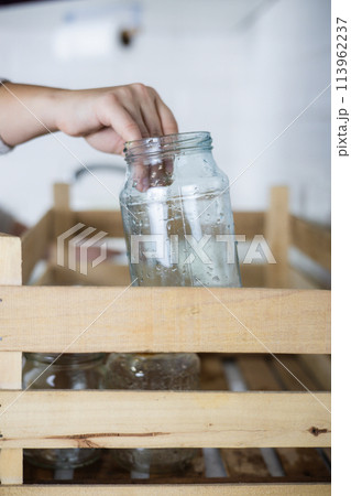 Vertical. A housewife reaches out and places an old glass jar in a recycling bin. A housewife collects unwanted glass jars and bottles at home to send for recycling. Glass recycling concept. 113962237