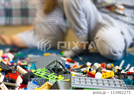 Against the background of a pile of construction sets, children assemble a toy. Children brother and sister enthusiastically assemble toys from construction set parts. 113962273
