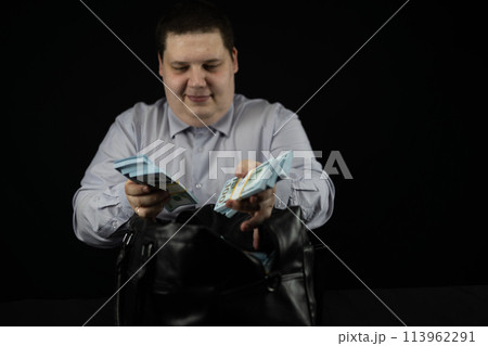 A man's hand takes stacks of dollars from a leather bag on a black background. A businessman takes money out of an open bag. Big money concept, bag with dollars. A man's hand takes stacks of dollars from a leather bag on a black background. A businessman takes money out of an open bag. Big money concept, bag with dollars. 113962291