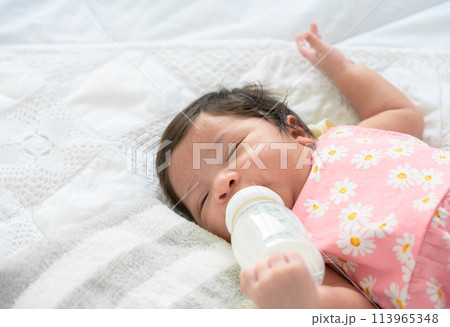 Newborn baby girl sleeping alone on bed and drinking milk from bottle 113965348
