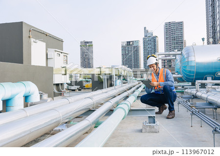 engineer male technician worker working service hotel boiler tank hot water supply pipe system. man safety checking maintenance pipeline heating water delivery line at roof top outdoor. 113967012