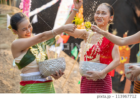 Songkran festival. Northern Thai people in Traditional clothes dressing splashing water together in Songkran day cultural festival with sand pagoda and colorful paper flag. Songkran festival. Northern Thai people in Traditional clothes dressing splashing water together in Songkran day cultural festival with sand pagoda and colorful paper flag. 113967712