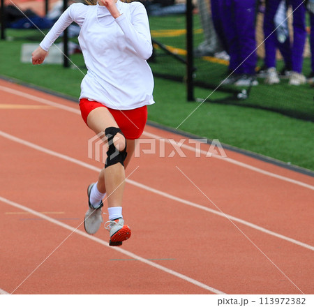 Ond girl running a sprint race on a track wearing KT tape on her knee Ond girl running a sprint race on a track wearing KT tape on her knee 113972382