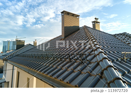 Closeup snow guard for safety in winter on house roof top covered with ceramic shingles. Tiled covering of building Closeup snow guard for safety in winter on house roof top covered with ceramic shingles. Tiled covering of building 113972720