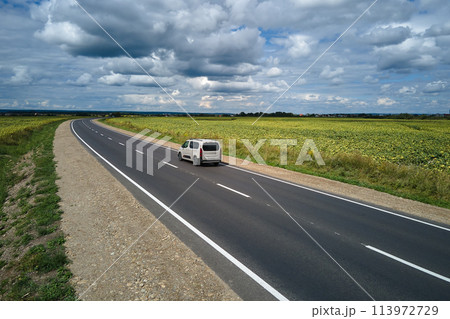 Aerial view of intercity road between green agricultural fields with fast driving car. Top view from drone of highway traffic 113972729