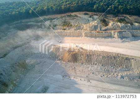 Aerial view of open pit mining site of limestone materials extraction for construction industry with excavators and dump trucks. Aerial view of open pit mining site of limestone materials extraction for construction industry with excavators and dump trucks. 113972753